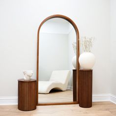 a large mirror sitting on top of a wooden table next to a vase and chair