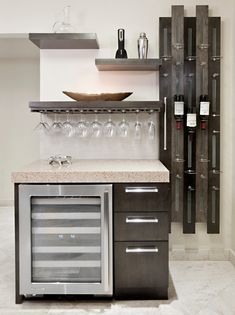 a kitchen with wine glasses on the counter and shelves above it that hold several bottles