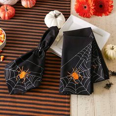 two napkins with spider web on them sitting on a table next to pumpkins