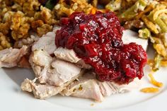 a white plate topped with turkey and cranberry sauce next to green beans, rice and stuffing