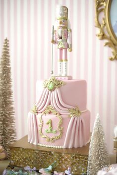 a pink and gold birthday cake with a nutcracker on top