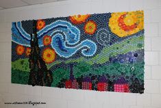 a painting made out of plastic bottle caps on a wall in a school hallway with white brick walls