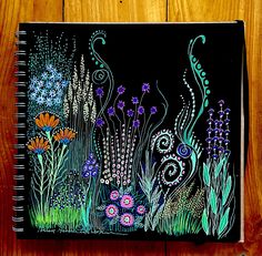 a notebook with an image of flowers and plants painted on the cover, sitting on a wooden surface