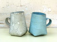 two ceramic mugs sitting next to each other on a white counter top in front of a brick wall