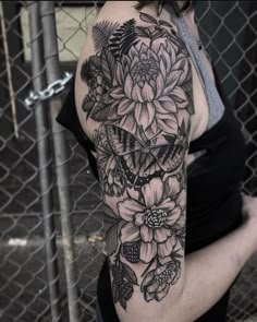 a woman with a black and white flower tattoo on her arm, standing in front of a chain link fence