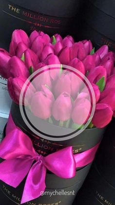 pink tulips are in a black box with a bow around the top and bottom