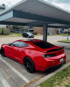 a red sports car parked in a parking lot next to a gas station with two cars