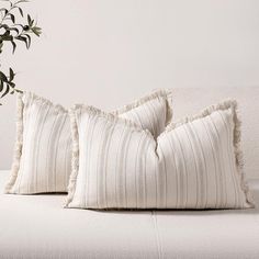 two white pillows sitting on top of a bed next to a plant in a vase