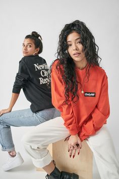 two women sitting on top of a skateboard wearing orange and black sweatshirts with the words new york city records printed on them