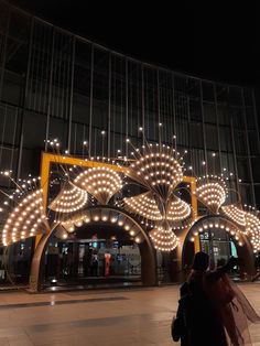 people are standing in front of a large building with lights on it's sides