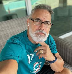 a man with glasses and a ring on his finger sitting in front of a couch