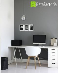 a desk with a computer on top of it and some pictures hanging up against the wall