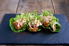 three lettuce wraps with meat and cole slaw on a black slate board