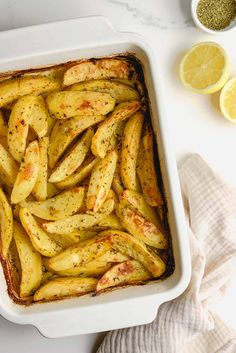 baked potatoes in a white casserole dish with lemons and seasoning on the side