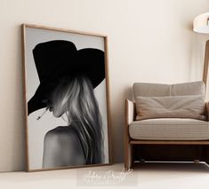 a black and white photo of a woman with long hair in a hat next to a chair