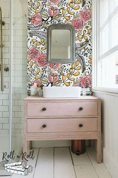 a bathroom with floral wallpaper and pink dresser in front of the mirror on the wall