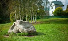 a large rock sitting in the middle of a lush green field next to a white house