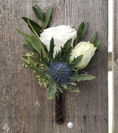 a boutonniere with white flowers and greenery on a wooden fence post