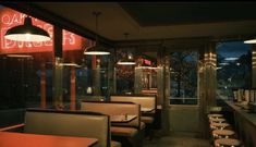 the interior of a restaurant with tables and stools in front of large windows at night