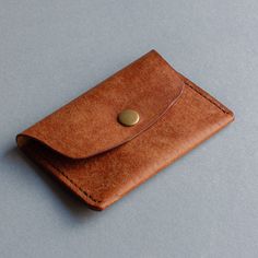 a brown leather wallet with a button on the front and side flap, sitting on a gray surface