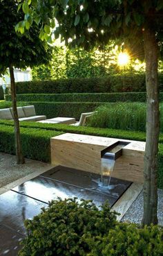 a water fountain in the middle of a garden with benches and trees around it,