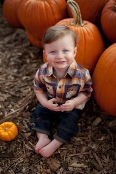 a little boy sitting on the ground in front of pumpkins with his eyes wide open