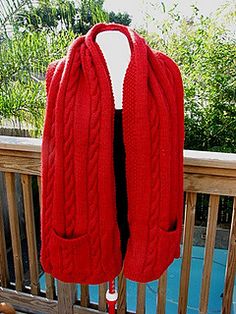 a woman's red cardigan sweater is hanging on a wooden rail with trees in the background