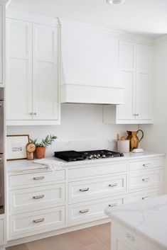 a kitchen with white cabinets and marble counter tops is pictured in this image, there are two vases on the stove top