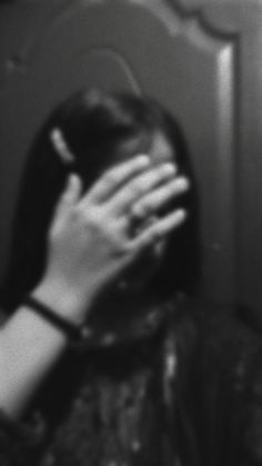 black and white photograph of woman covering her face with hands in front of wall mirror