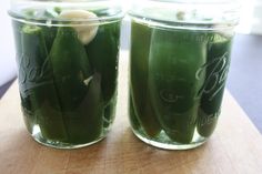 two jars filled with pickles sitting on top of a wooden table next to each other