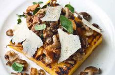 a white plate topped with lots of food on top of a wooden table next to mushrooms and parmesan cheese