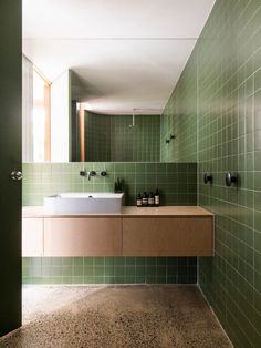 a green tiled bathroom with two sinks and mirrors