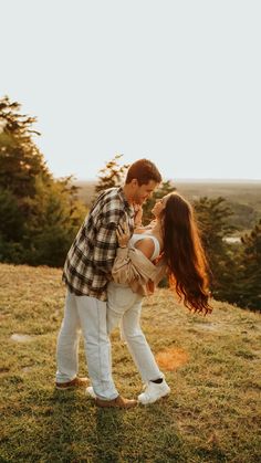 a man and woman standing on top of a grass covered field next to trees in the background