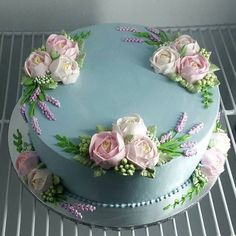 a blue cake decorated with pink flowers on top of a cooling rack in a kitchen