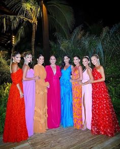 a group of women standing next to each other on a wooden platform in front of palm trees