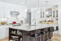 a large kitchen with white cabinets and marble counter tops, along with bar stools