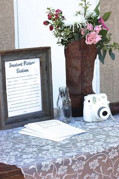 a table topped with a vase filled with flowers next to a camera and framed sign