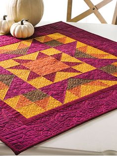 a table topped with a purple and yellow quilted placemat next to two white pumpkins