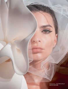 a woman wearing a white veil over her head with a flower in front of her face