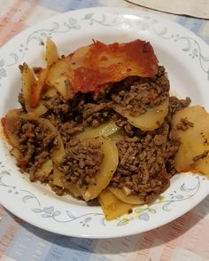 a white plate topped with meat and potatoes on top of a checkered table cloth