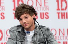 a young man sitting at a table with a microphone in front of his ear and wearing a denim jacket