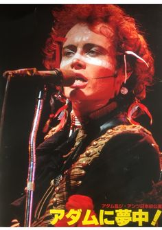 a man with red hair and piercings on his head is singing into a microphone