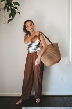 ashley wearing a white and navy striped top, brown drapey pants, brown leather sandals, a tan woven tote bag, and tan frame sunglasses Cool Mum Outfit Summer, Mum Fashion 2024 Summer, Boho Mom Outfits, Striped Tank Top Outfit, Goal Outfits, Brown Linen Pants, 2024 Clothes, Minimalist Fashion Summer, Mom Style Summer