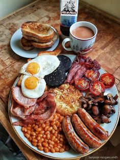 a breakfast plate with eggs, sausages, beans and toast on it next to a cup of coffee