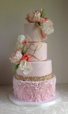 a three tiered pink cake with flowers on the top and gold trimmings