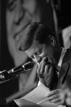 black and white photograph of a man holding his hand to his face while reading a paper