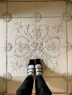 someone wearing black and white striped shoes standing in front of a wall with floral designs on it