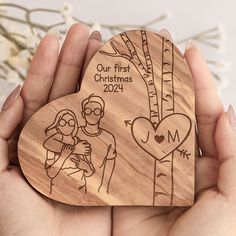 two hands holding a wooden heart shaped ornament with an image of a man and woman