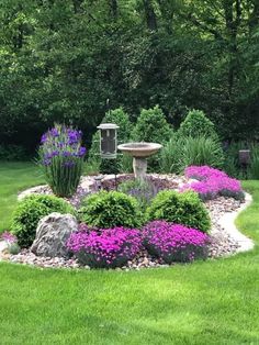 a birdbath in the middle of a garden with purple flowers and rocks around it