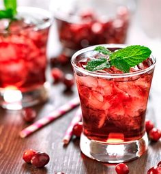 two glasses filled with ice and cranberries on top of a wooden table next to candy canes